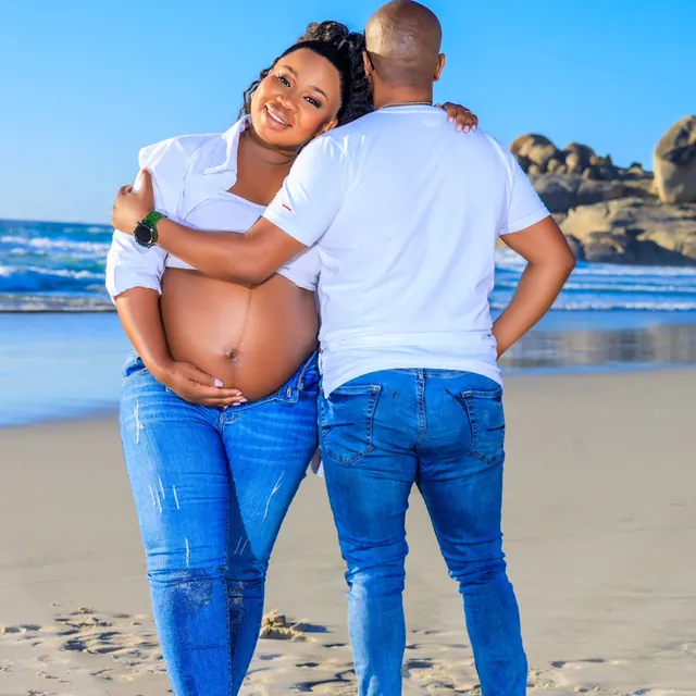 Maternity couple embracing on a beach with large boulders