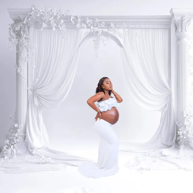Maternity session in an elegant white gown, draped archway backdrop